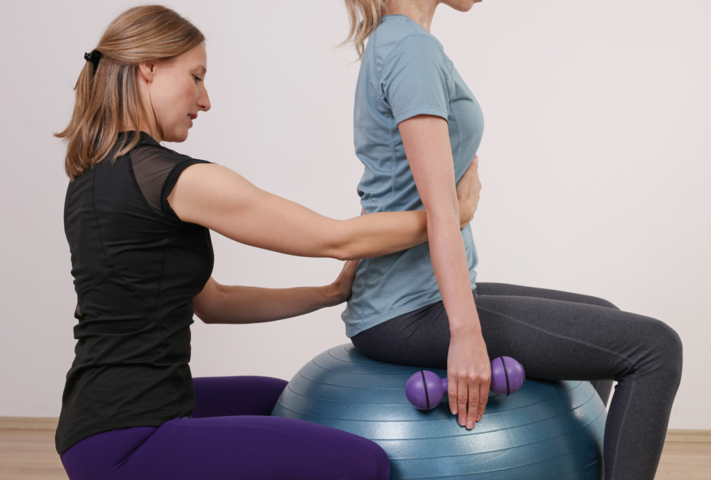 Physiotherapist teaching Pilates to a patient sitting on a stability ball.